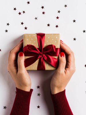 Woman hands holding christmas holiday gift box on decorated festive table with sparkle stars on white background. Packaging gift wrap